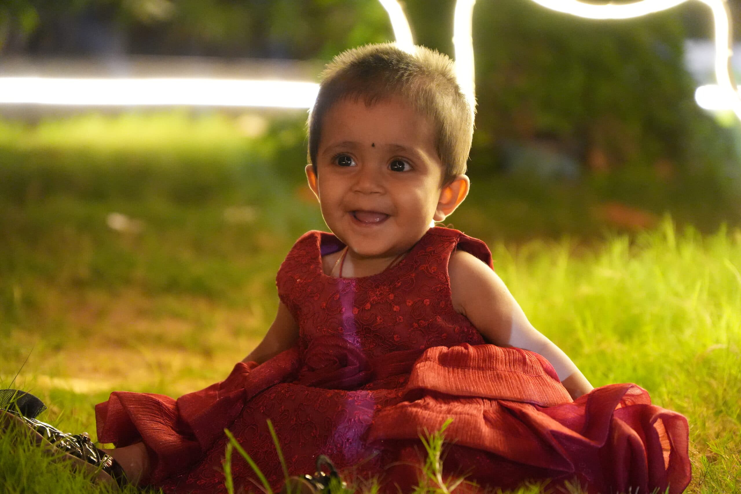 A little girl smiling on the grass in a red dress